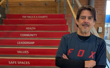 older adult male stands in front of red steps inside a building