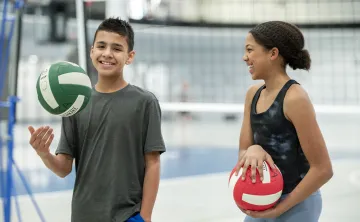 Youth holding volleyballs and smiling in a gymnasium