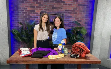 Two women smiling behind a table of camping supplies